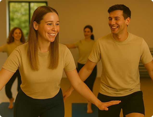 Four people smiling and balancing on one leg during a yoga class in a bright room.