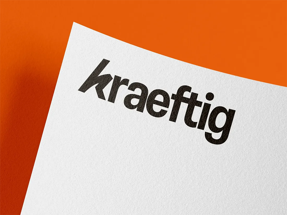 Das Wort 'kraeftig' in fetter schwarzer Schrift auf weißem Papier vor orangefarbenem Hintergrund.