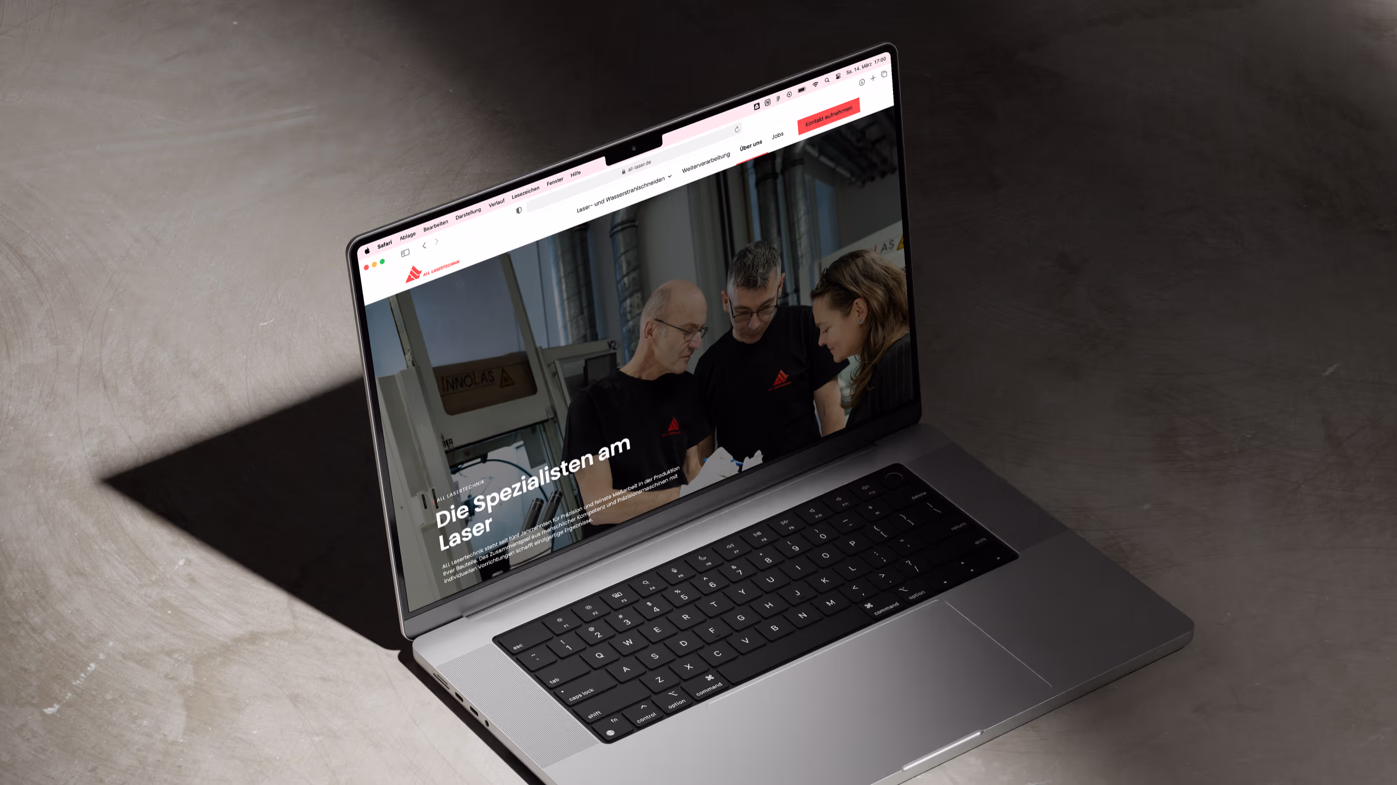 Laptop mit geöffneter Webseite über Laserspezialisten, zeigt drei Personen bei der Arbeit in einer Werkstatt.