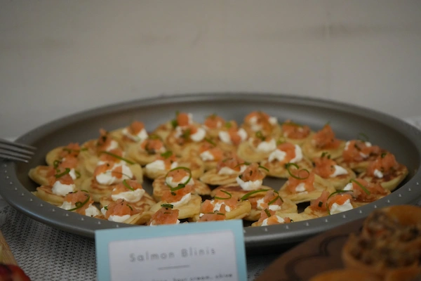 A platter of bite size blinis (buckwheat pancakes), topped with creme fraiche, slivers of smoked salmon, and finely sliced chives