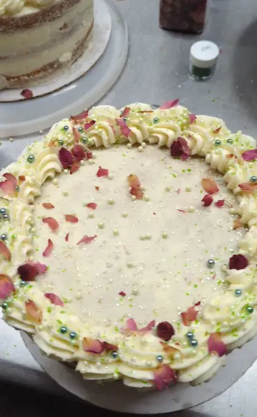 The top view of a champagne and rose cake, covered with a cream colored buttercream, and sprinkled with dried rose petals and a variety of complimentary sprinkles and glitter
