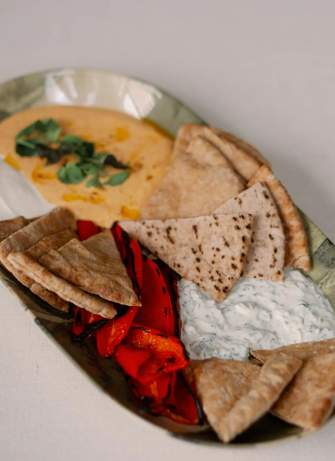 Brown pita slices rest on a serving platter between pools of white and orange whipped feta and roasted red peppers