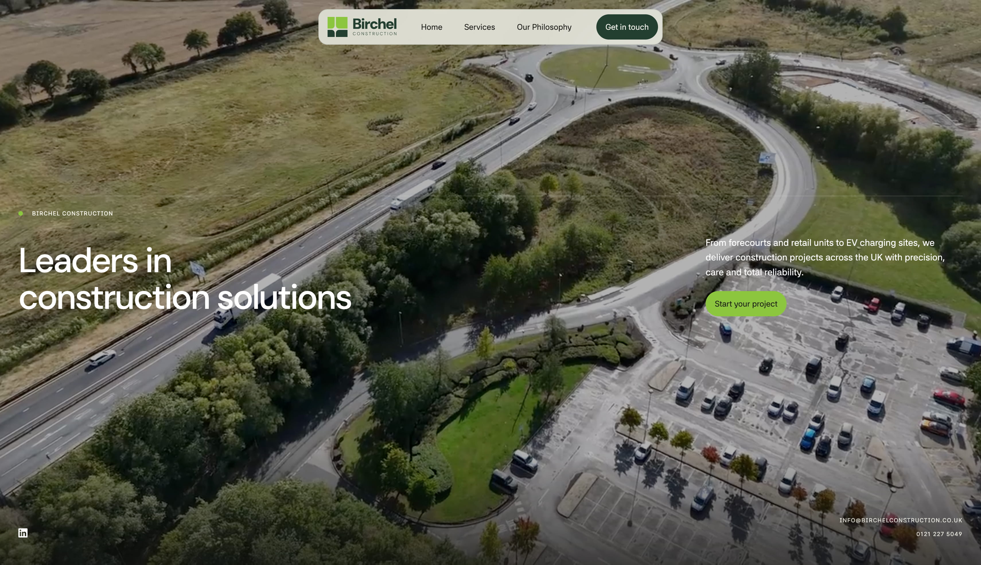 Aerial view of a curved road, roundabout, and parking lot surrounded by green trees and fields, with overlaid website text promoting Birchel Construction as leaders in construction solutions in the UK.