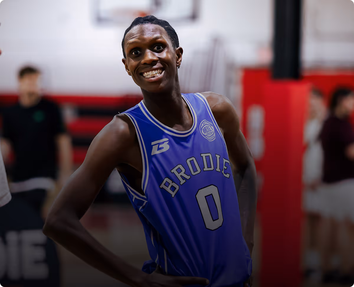 Smiling basketball player in a blue Brodie jersey with number 0 stands on court indoors.