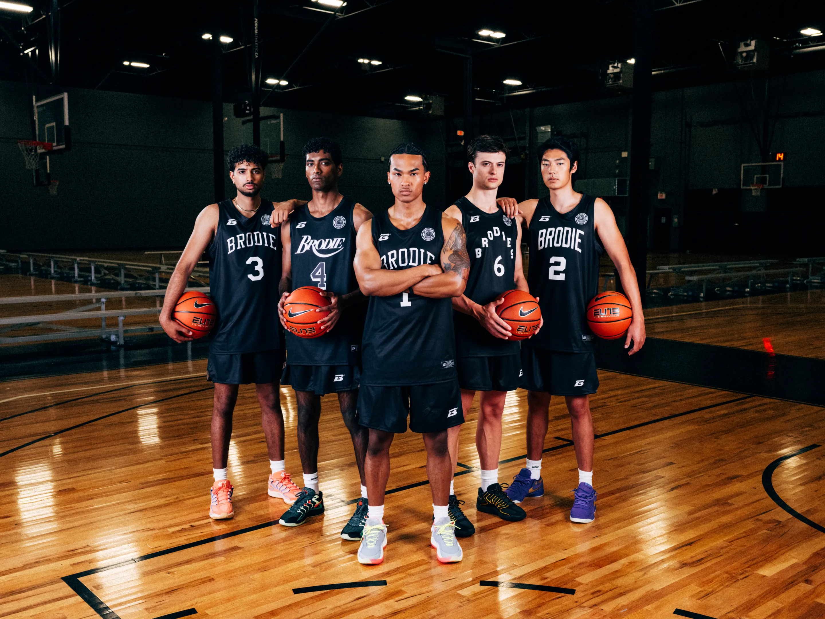 Five Brodie athletes in black jerseys holding basketballs on court