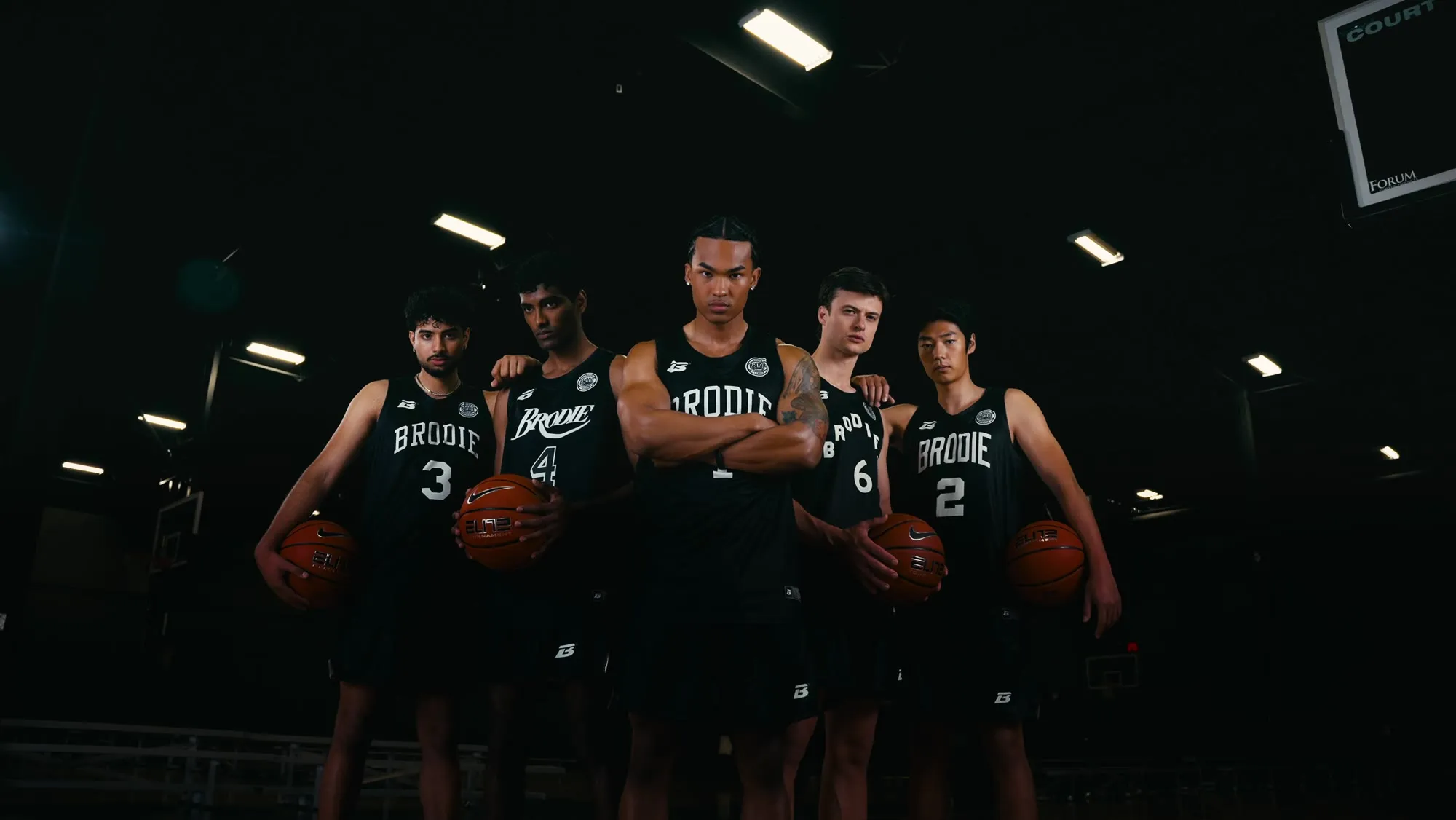 Five Brodie athletes in black jerseys holding basketballs in a gym