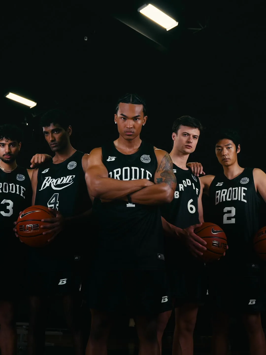 Five Brodie athletes in black jerseys holding basketballs in a gym