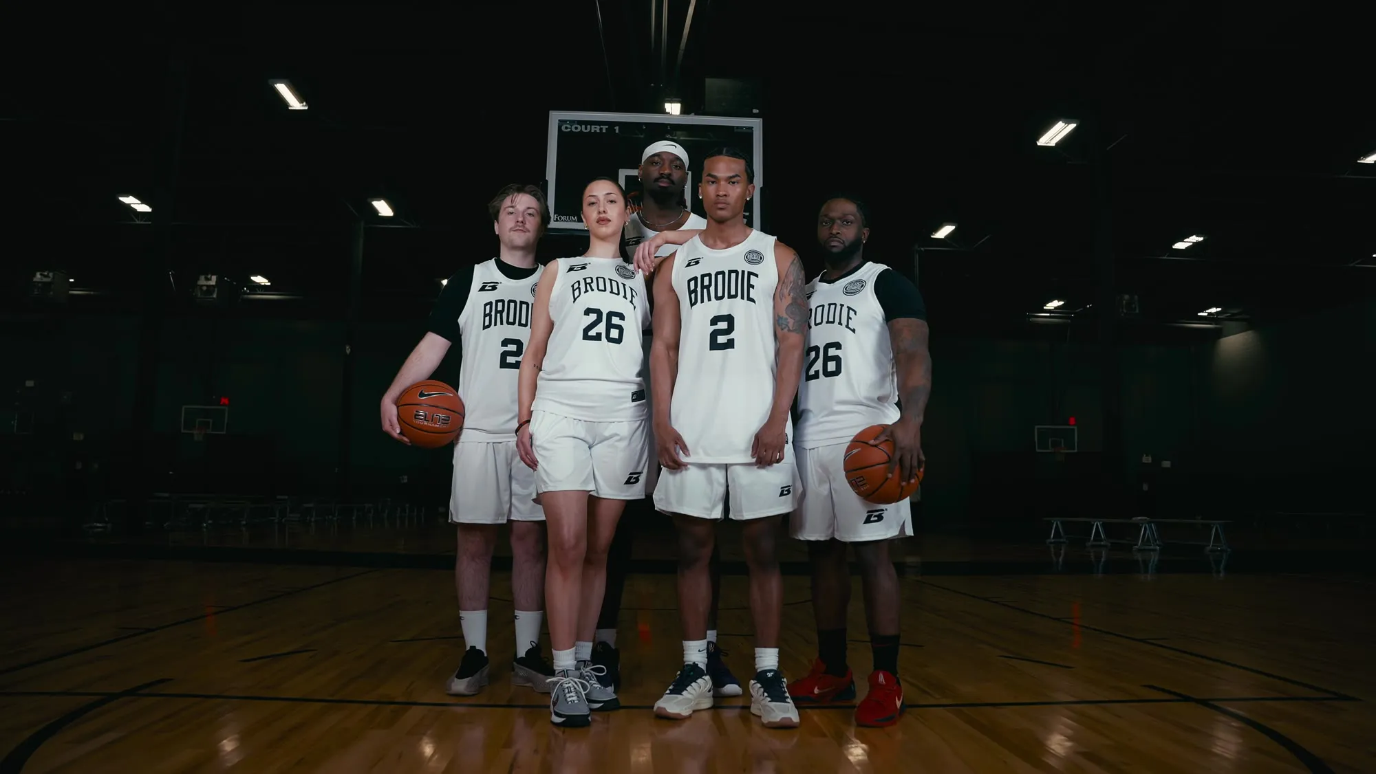 Five Brodie athletes in white jerseys standing together on court
