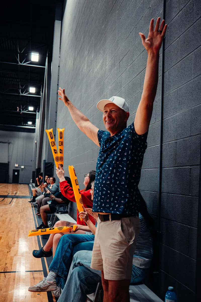 Fan cheering courtside with both arms up at a BRODIE game