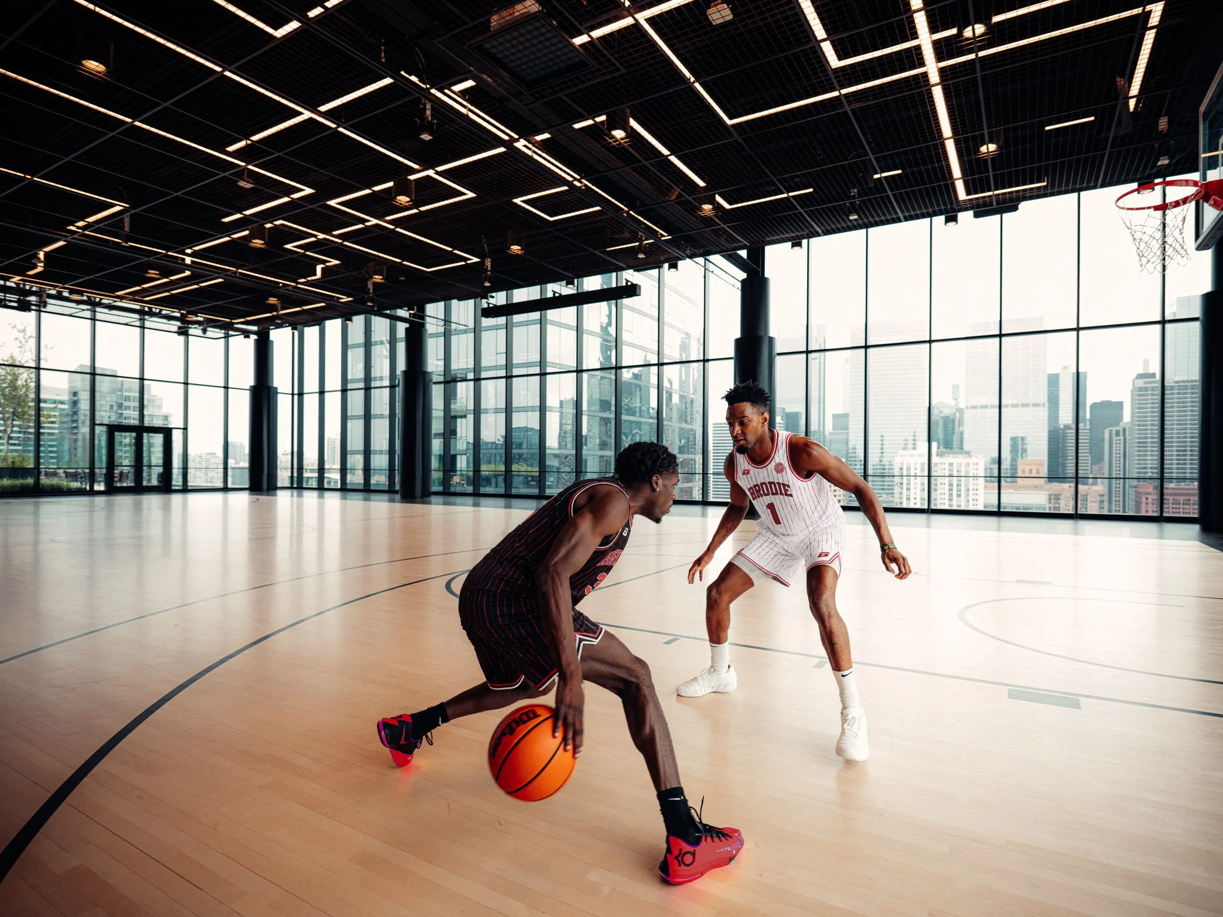 Two BRODIE players going one-on-one in a glass-walled gym above the city