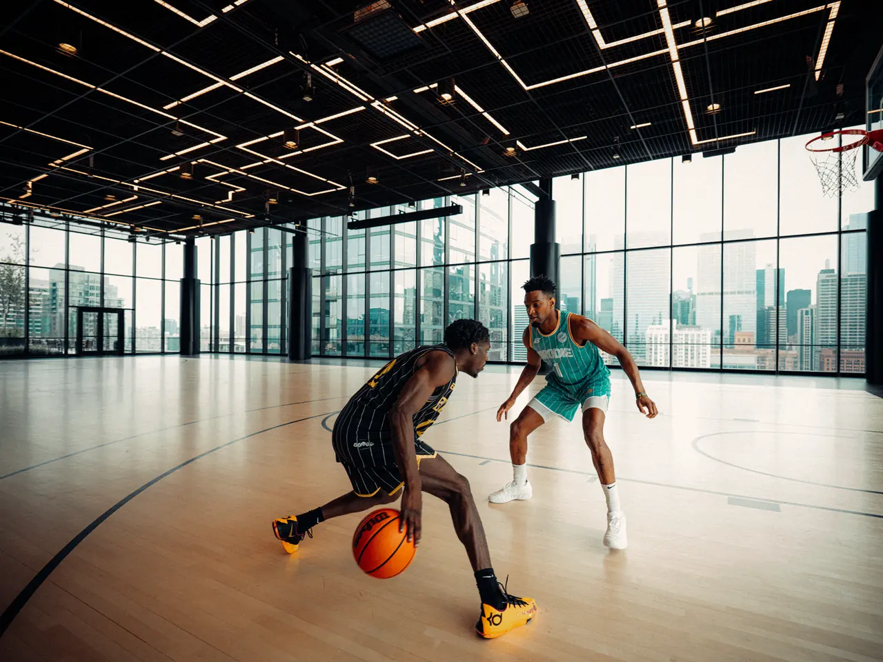 Two BRODIE players going one-on-one in a glass-walled gym above the skyline