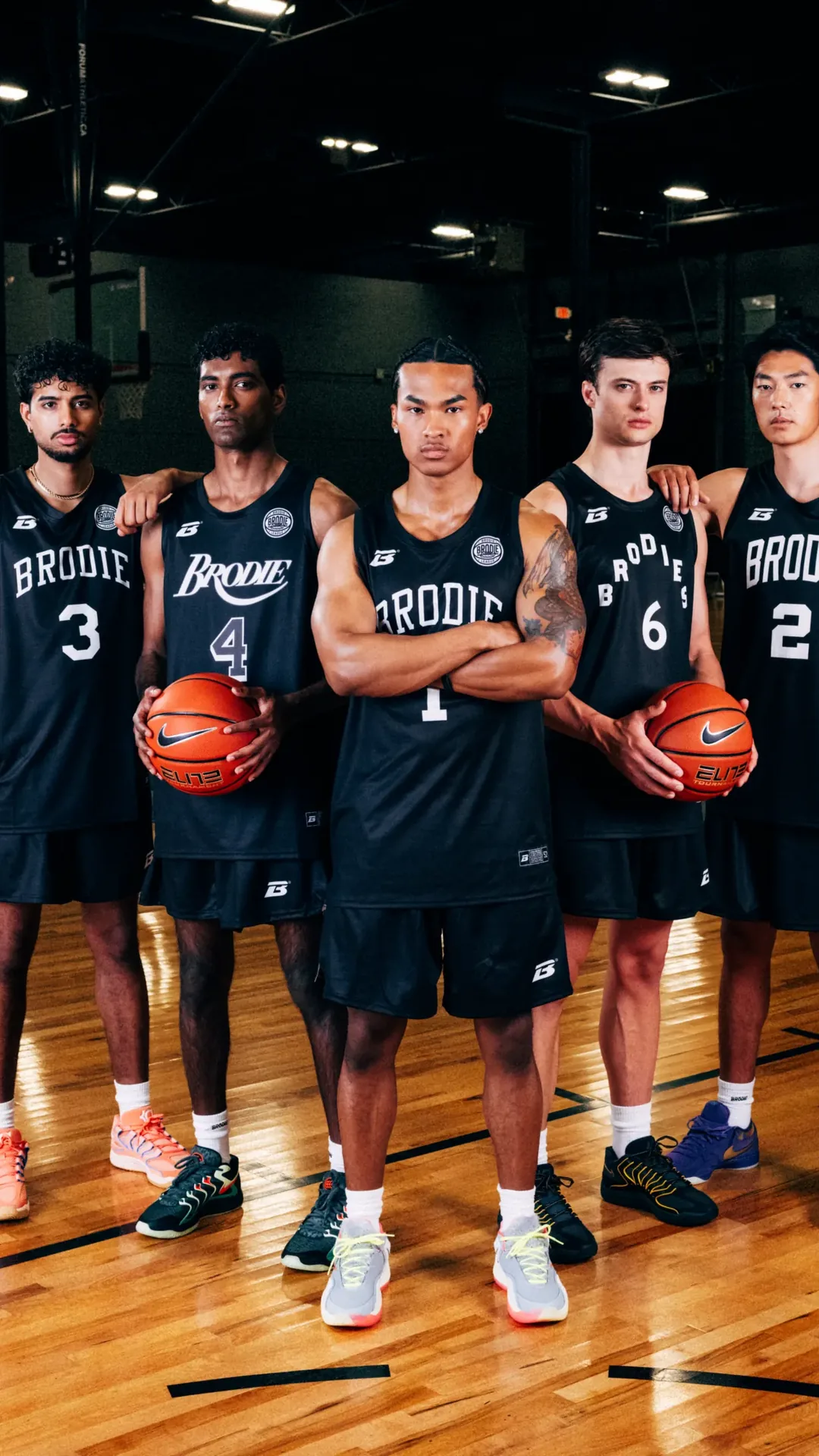 Five Brodie athletes in black jerseys holding basketballs on court