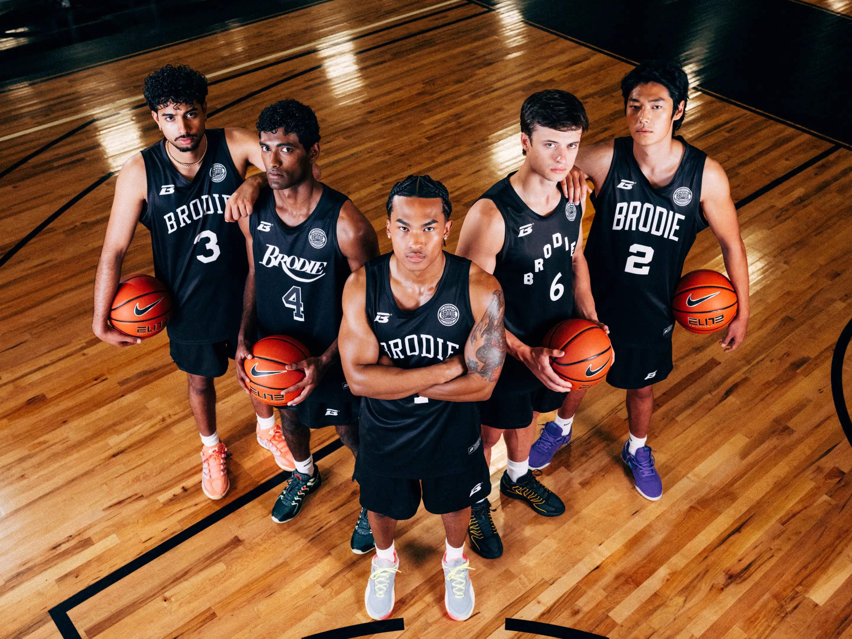 Five BRODIE® athletes in black jerseys holding basketballs on a hardwood court