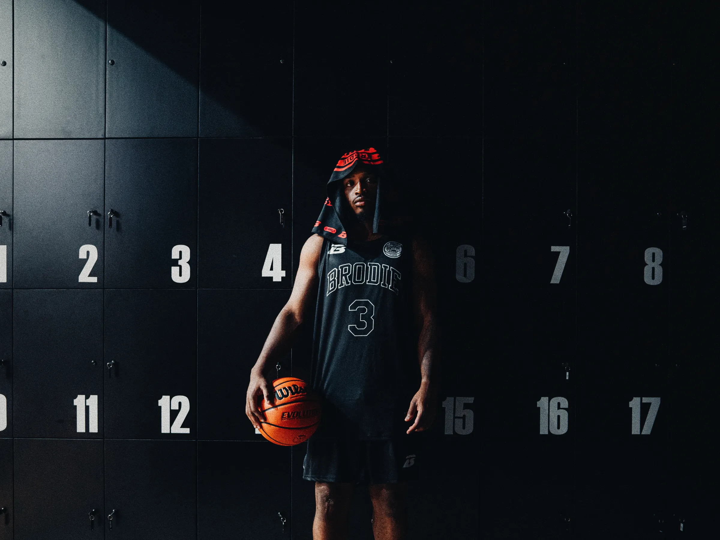 A BRODIE® athlete in a black number 3 jersey holding a basketball in front of numbered lockers