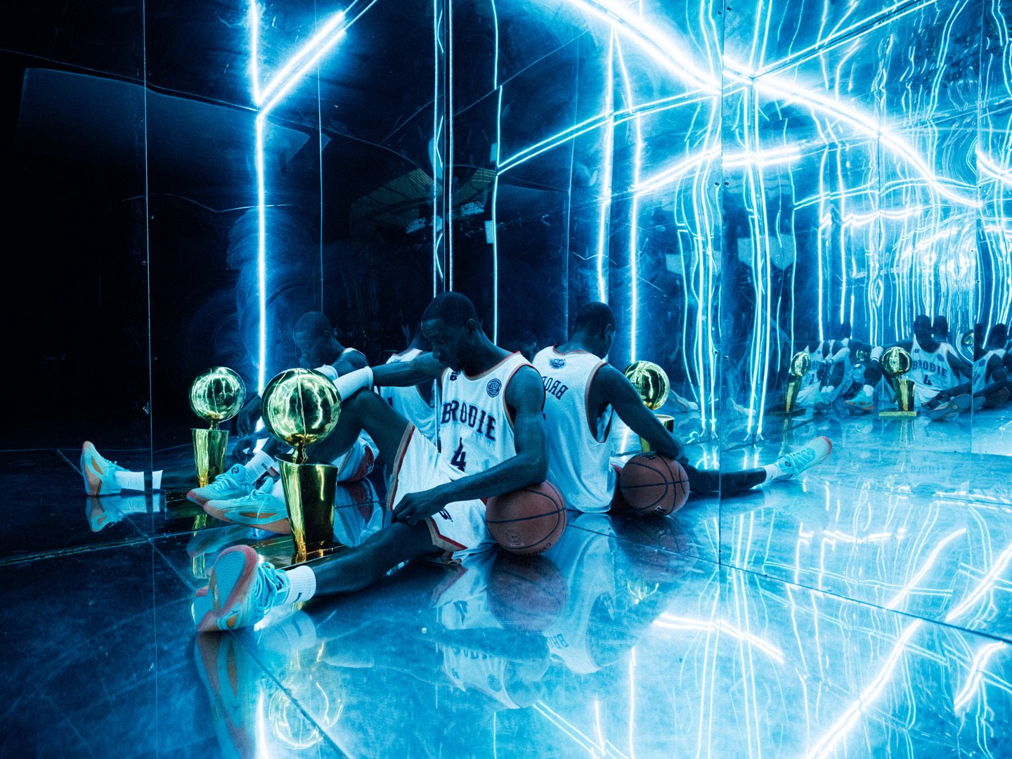 Two Brodie athletes sitting in a mirrored room lit by blue neon with championship trophies