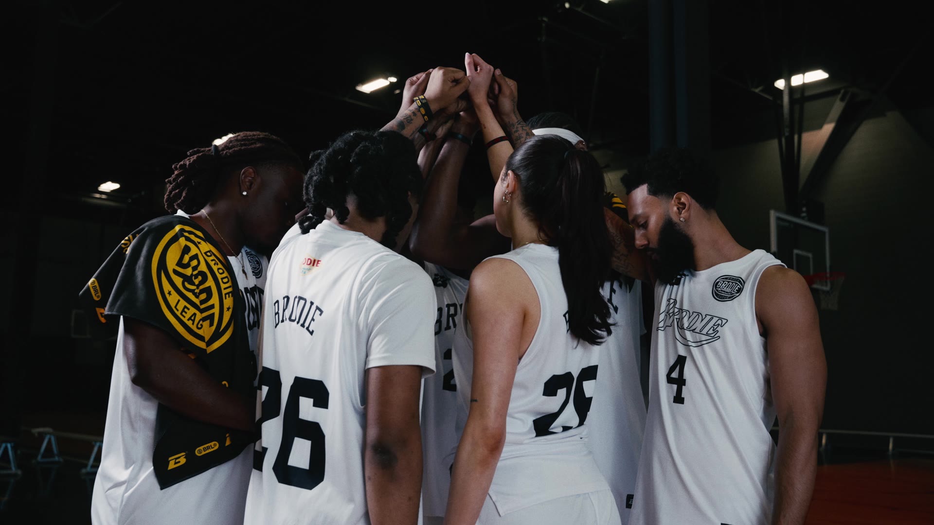 Brodie team in a huddle with hands raised together on court