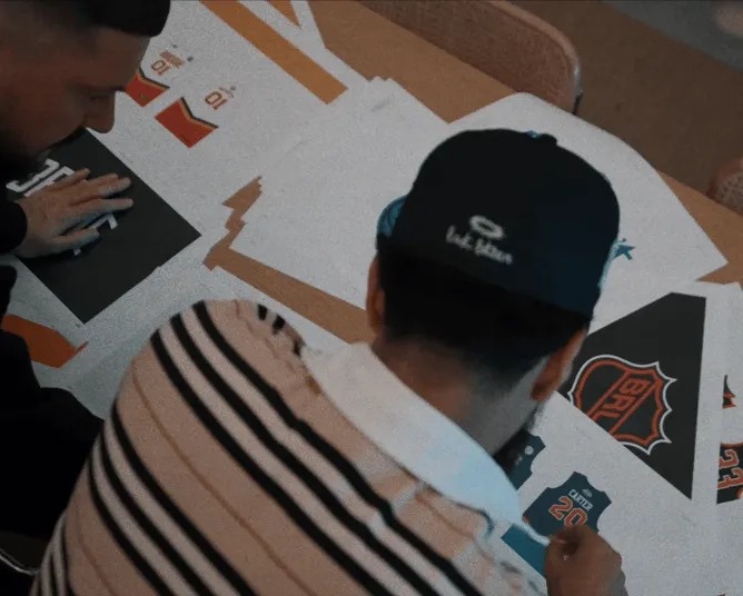 Overhead view of a team member in a cap looking over printed designs on a table