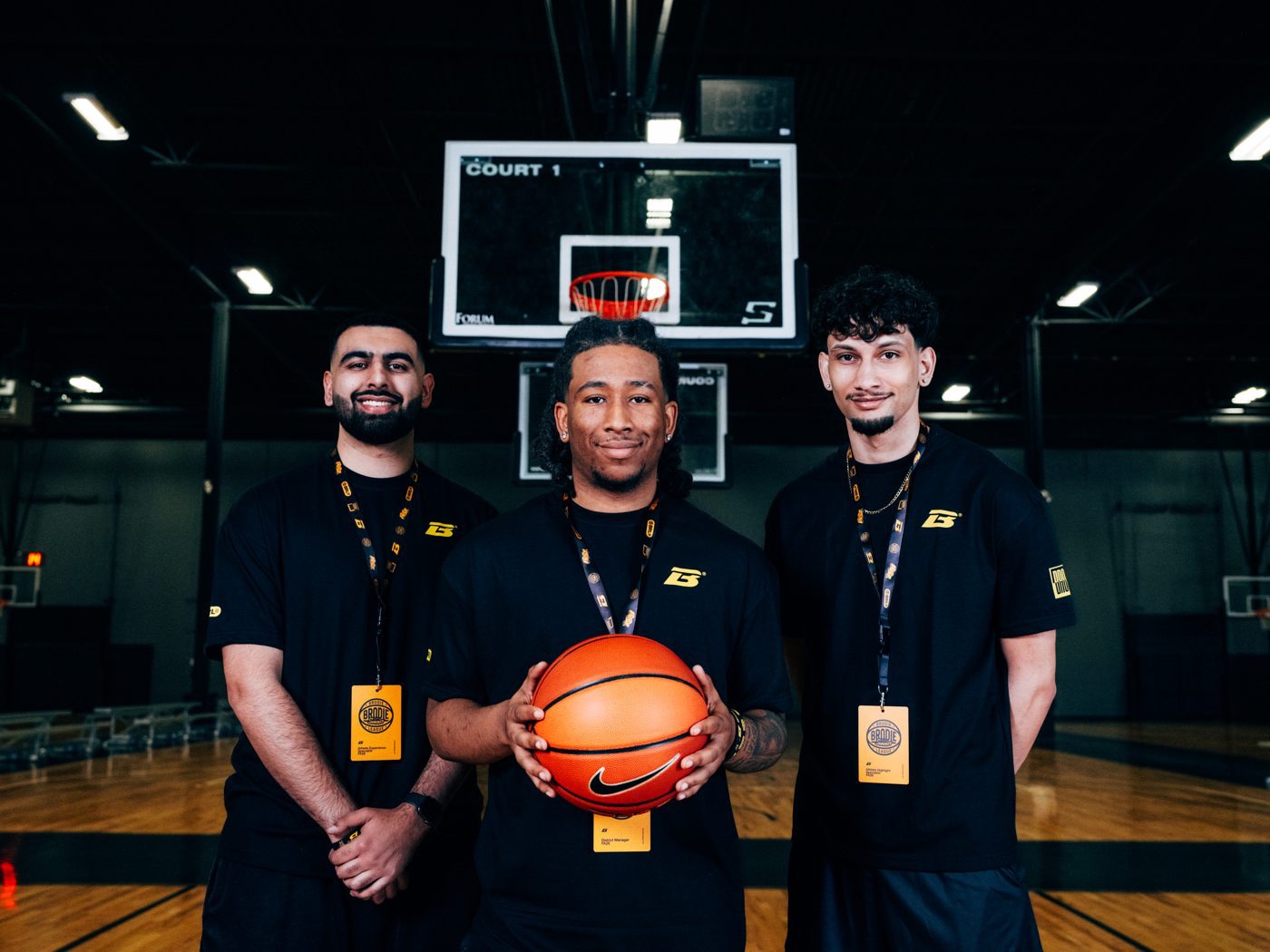 Three Brodie team members in black shirts posing with a basketball on court