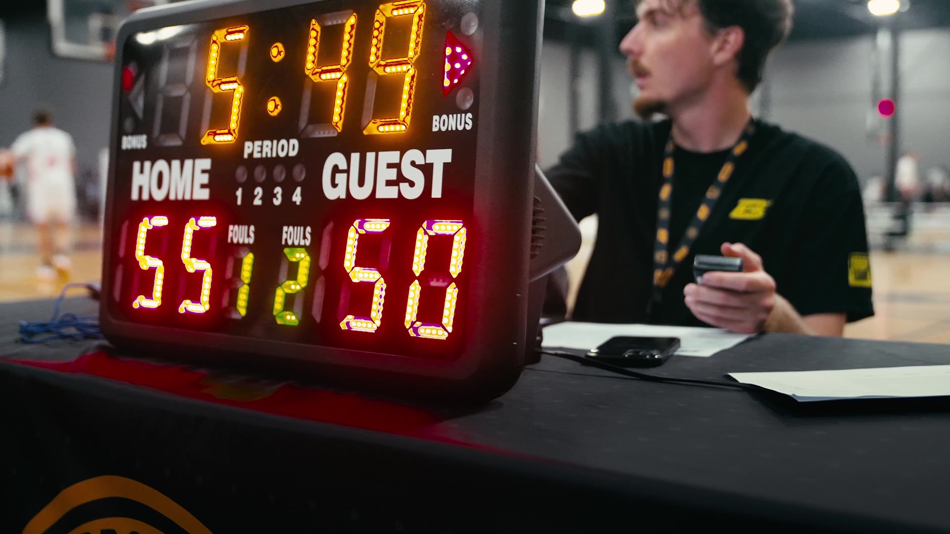 Brodie scorekeeper at the table beside the glowing scoreboard