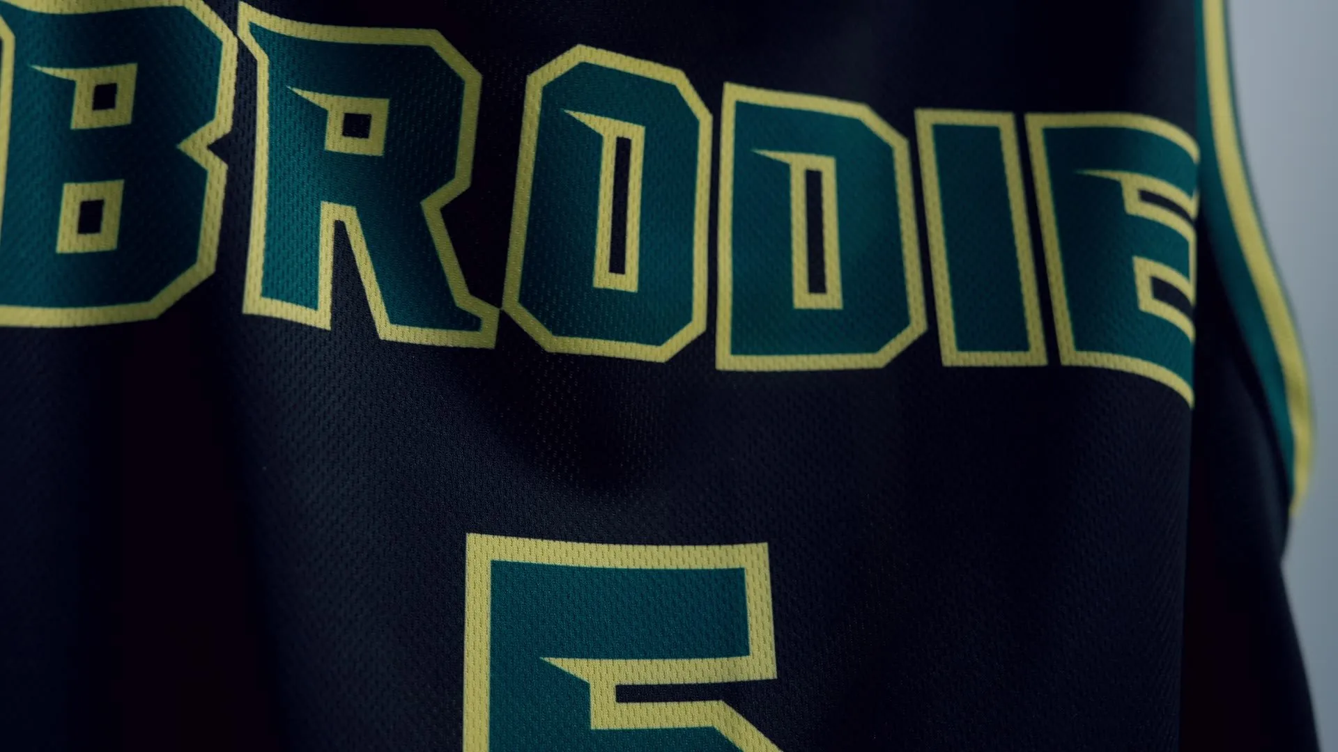 Close detail of a dark green Brodie jersey with gold outlined lettering