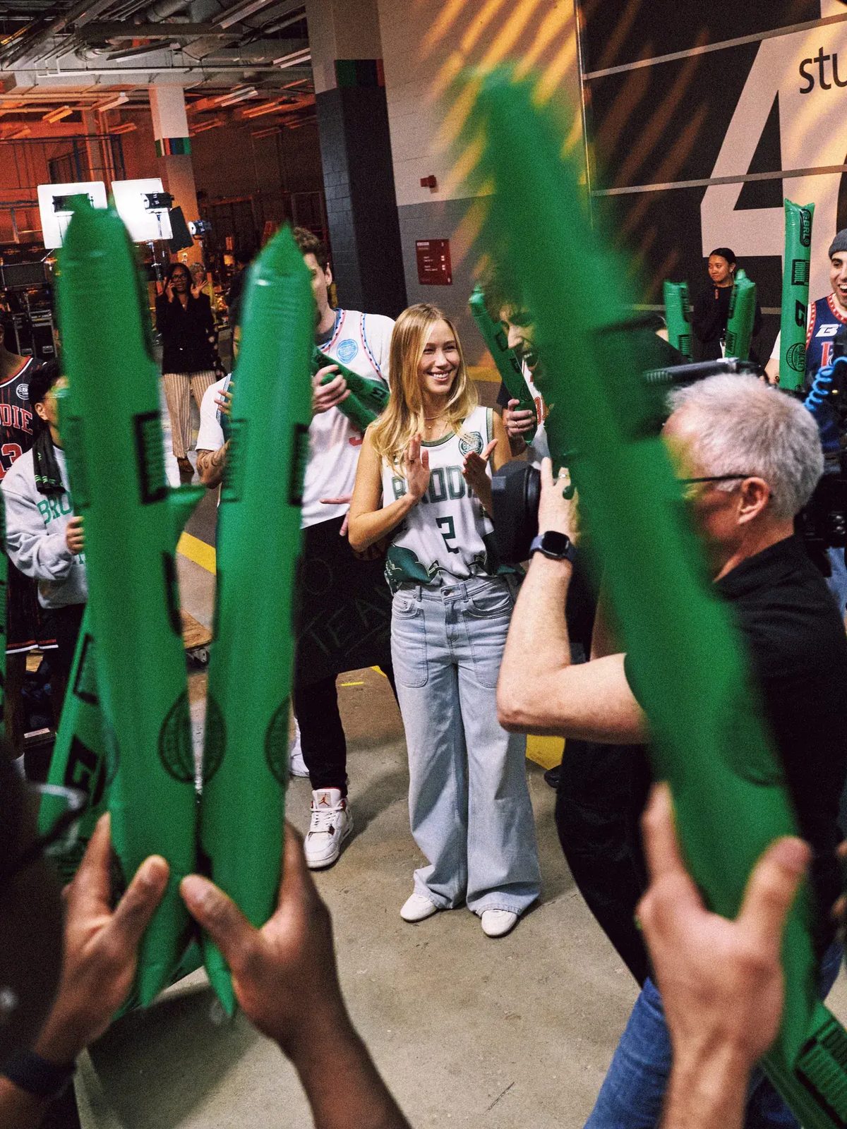 Athlete in a Brodie jersey smiling as teammates cheer with green thundersticks backstage