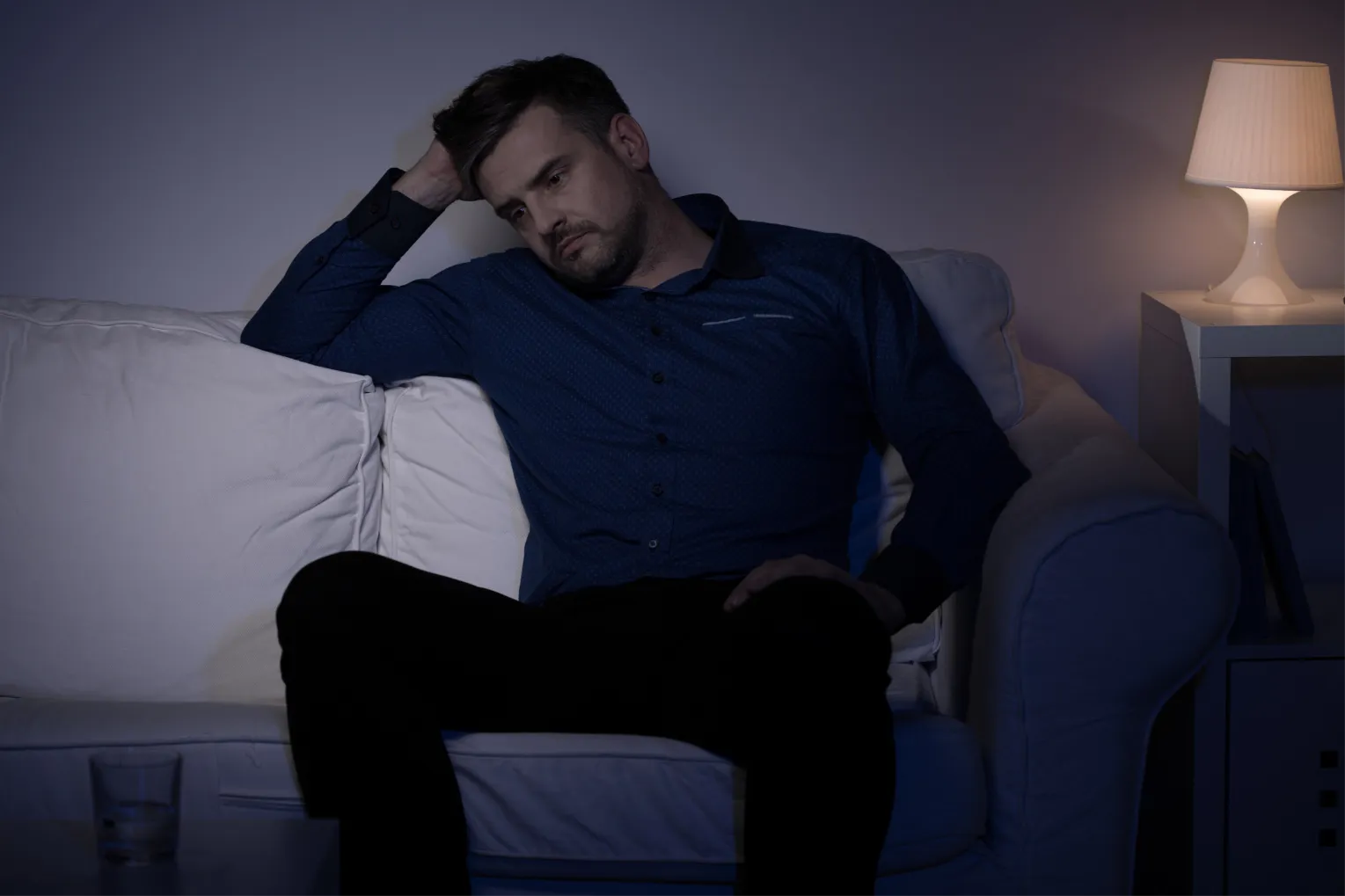 Mann sitzt nachdenklich in dunklem Wohnzimmer