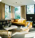 Bright mid-century modern living room with yellow sofa, wooden furniture, large windows, and natural light.