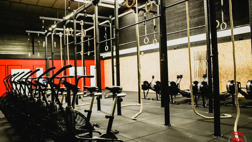 Interior of a CrossFit gym with air bikes, rowing machines, climbing ropes, and gymnastic rings.