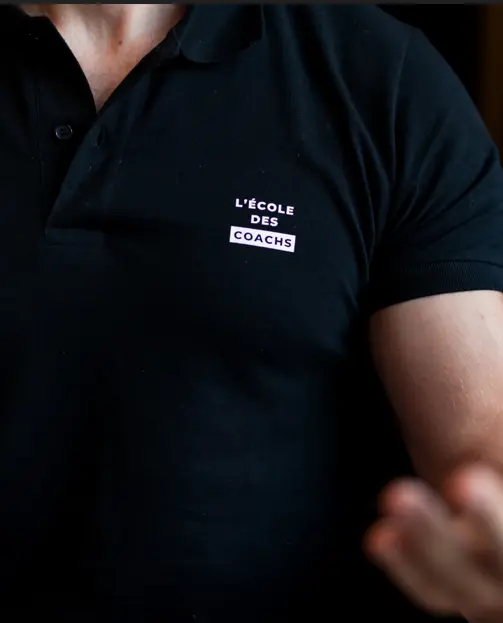 Person wearing a black polo shirt with white text 'L'ÉCOLE DES COACHS' on the chest.