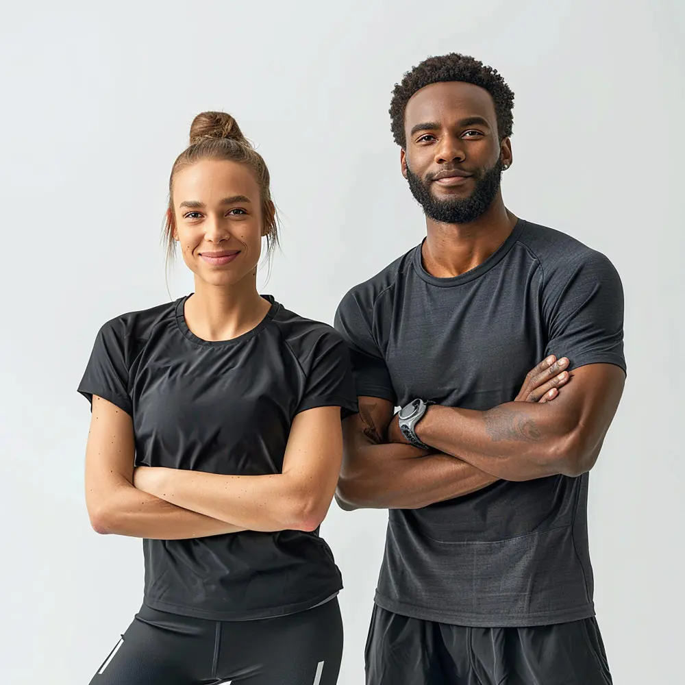 Confident young man and woman in black athletic wear standing with arms crossed against a plain white background.