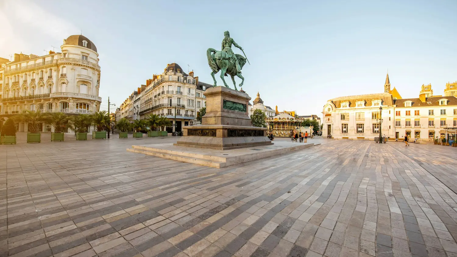 Equestrian statue of a rider holding a sword in a spacious town square with historic buildings and a carousel.