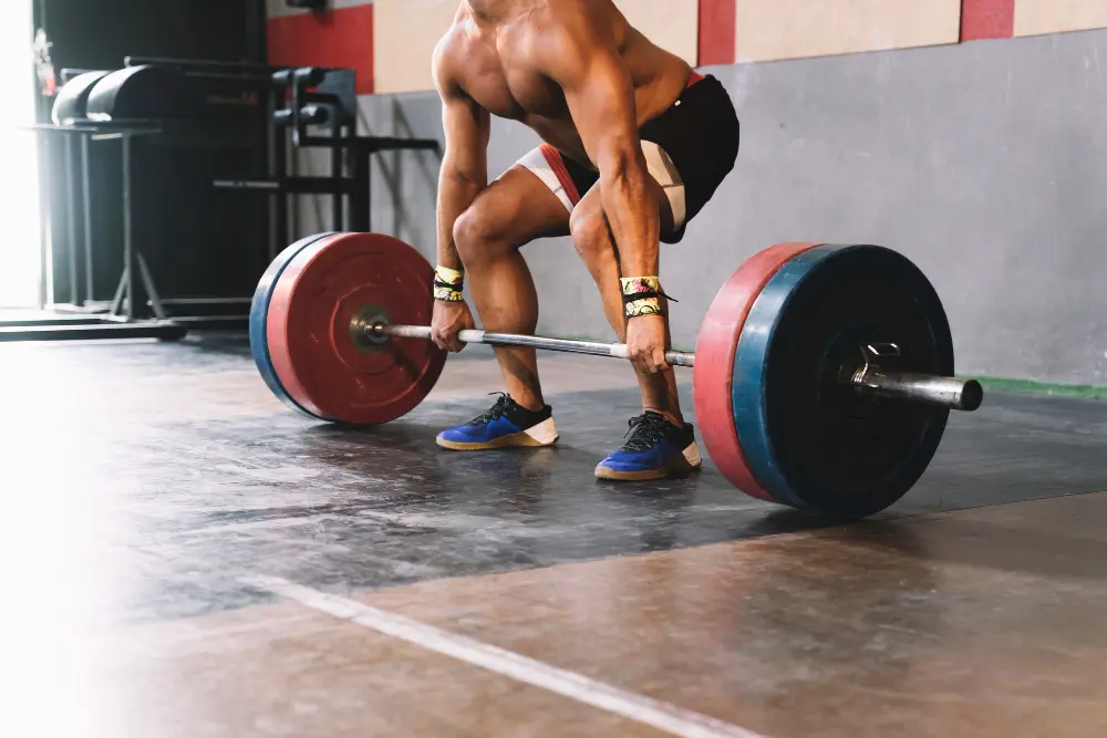 Muscular man in shorts and wrist wraps preparing to lift a heavily weighted barbell in a gym.