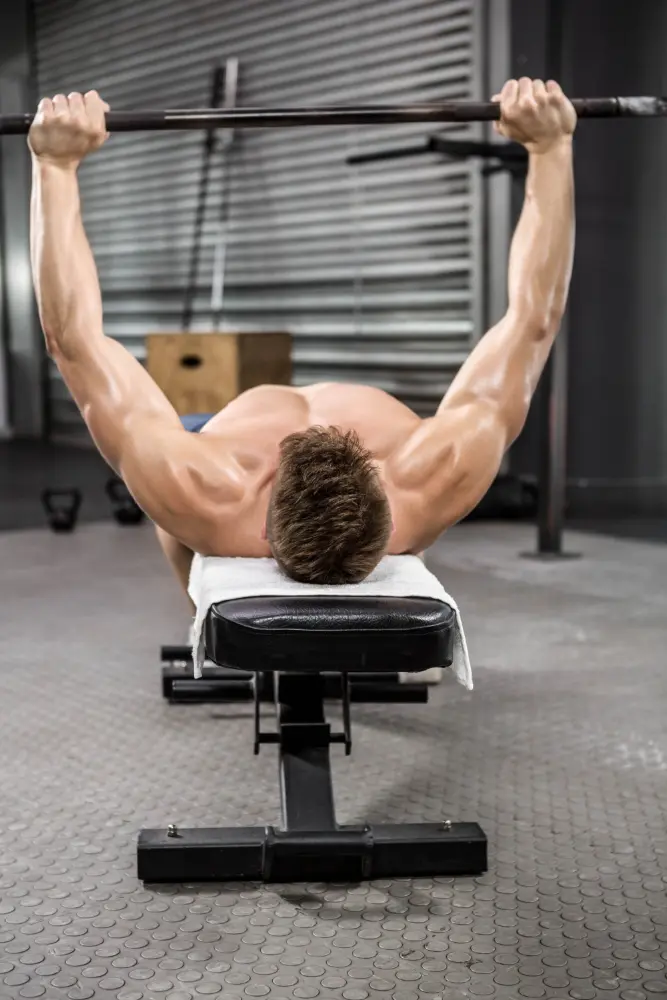Muscular man lying on a gym bench pressing a barbell overhead.