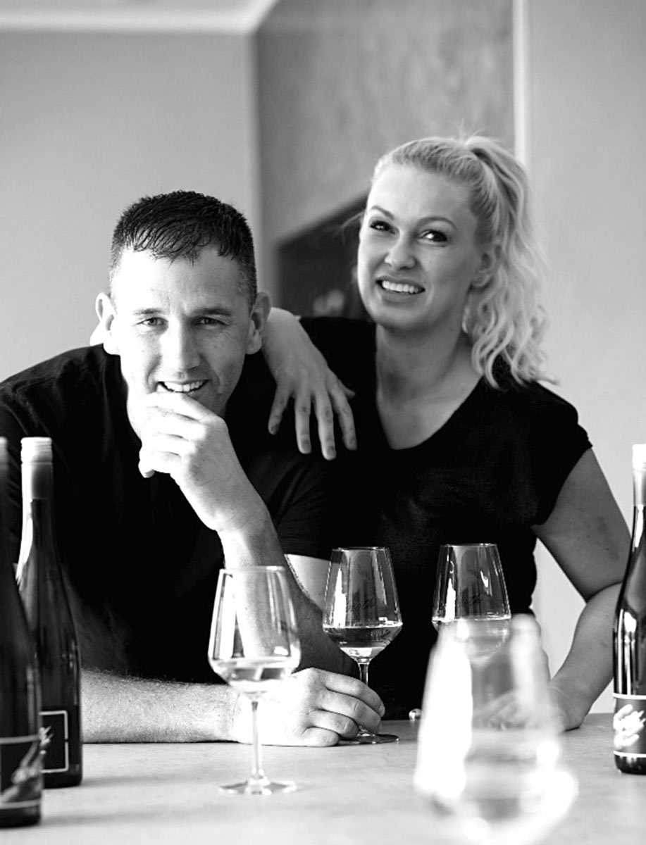 Michael Schroth und seine Frau zusammen an einem Tisch, mit zwei Weingläsern und zwei Flaschen Wein vom Weingut Schroth vor ihnen.