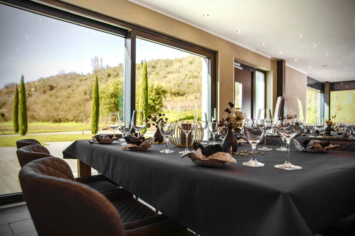 Eleganter Tisch mit schwarzem Tischtuch, Wein- und Wassergläsern sowie dekorativen Trockenblumen vor großen Fenstern mit Blick auf Weinberge im Weingut Schroth in Asselheim Pfalz.