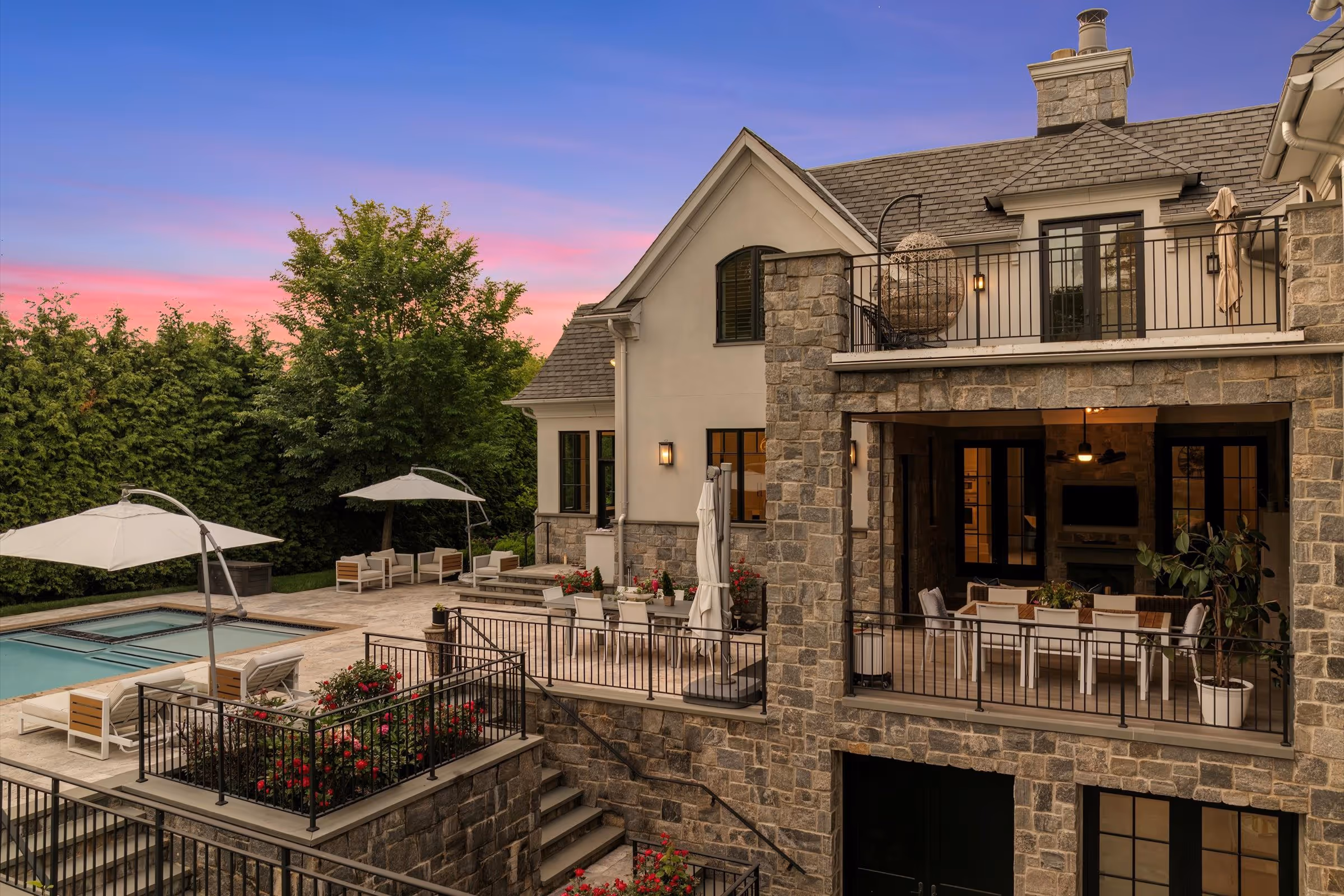 Stone and stucco house with outdoor patio, garden seating, and a swimming pool at sunset.