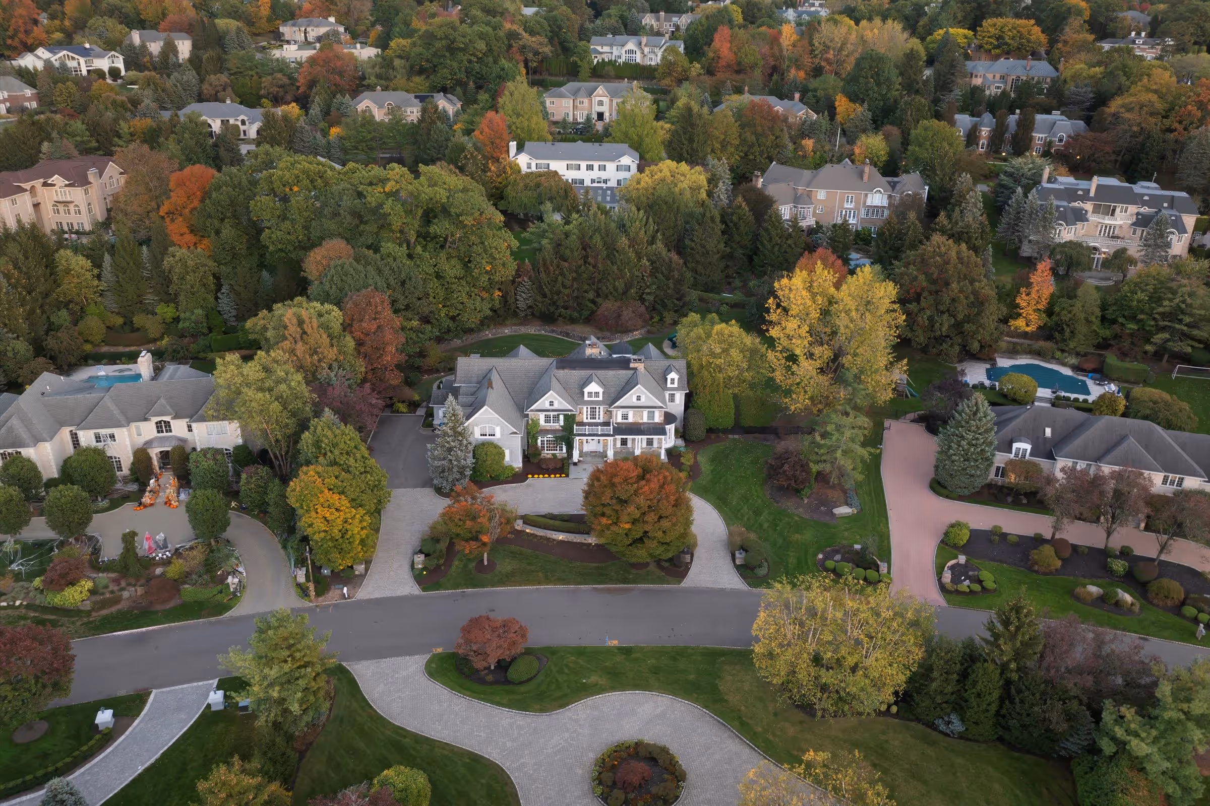 Aerial view of a suburban neighborhood with large homes surrounded by lush trees showing fall colors.