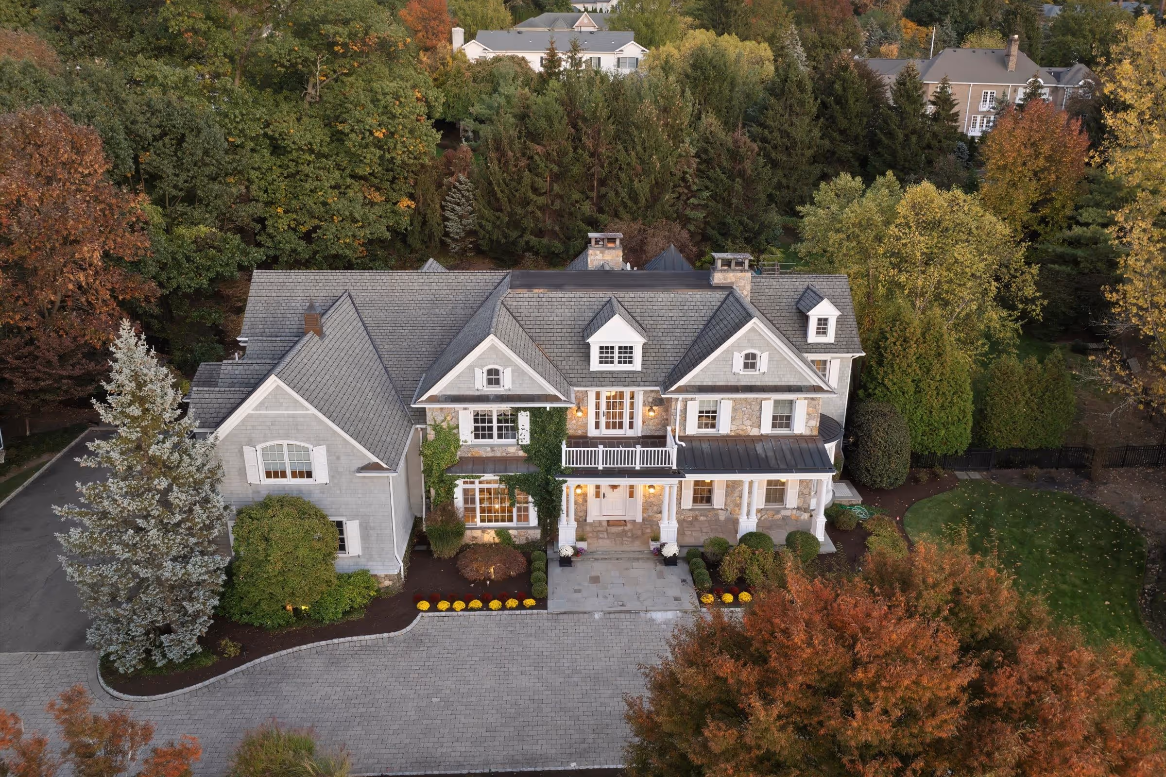 Large two-story gray stone house with white trim, surrounded by autumn trees and a paved driveway.