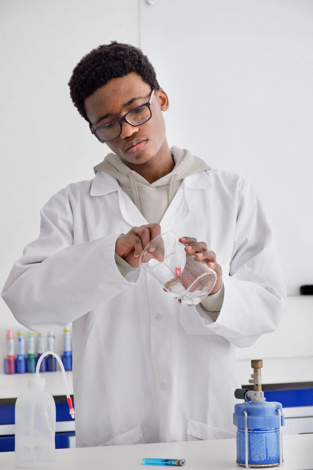 ESCA student in a white lab coat and glasses holding a glass beaker in a science lab.