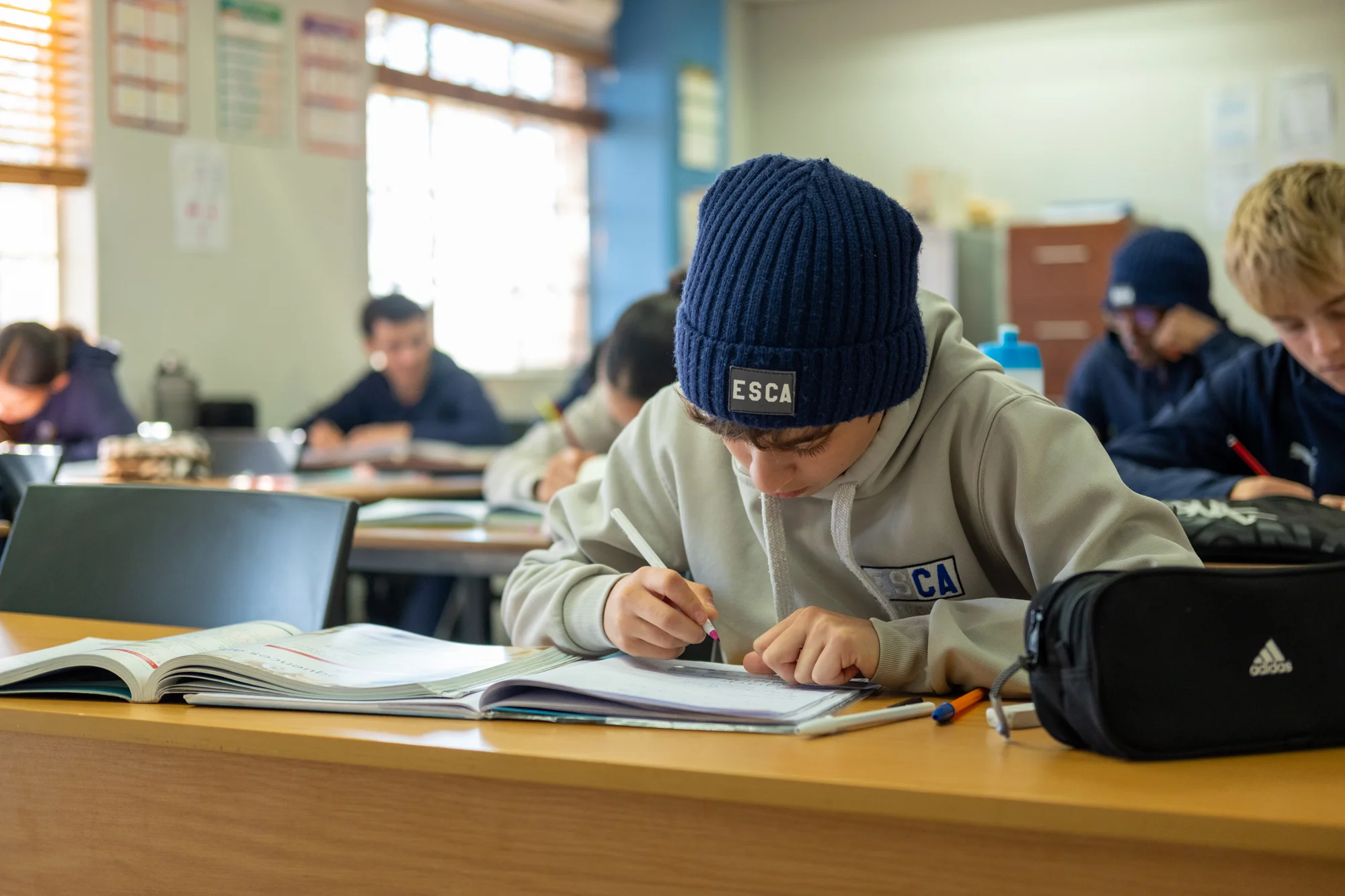 Five boys in white t-shirts and navy shorts standing closely with arms around each other, smiling outdoors on a sunny day.