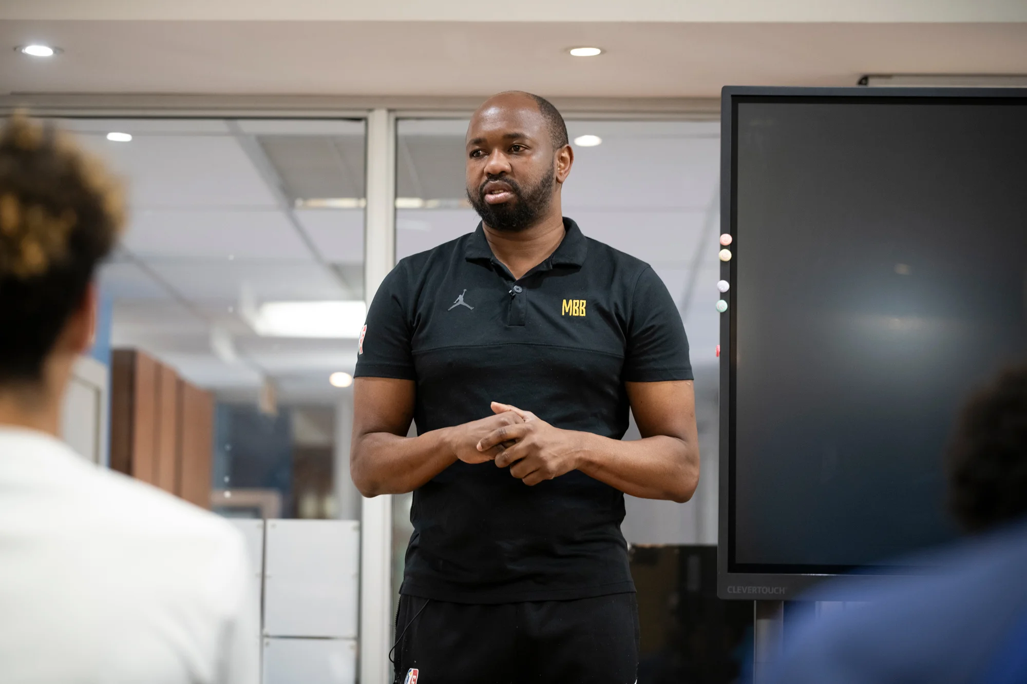 Five boys in white t-shirts and navy shorts standing closely with arms around each other, smiling outdoors on a sunny day.