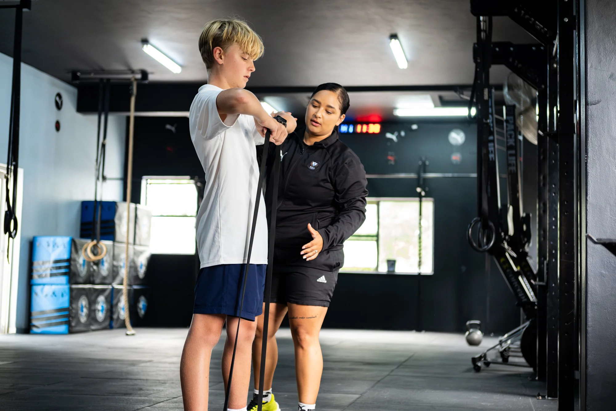Five boys in white t-shirts and navy shorts standing closely with arms around each other, smiling outdoors on a sunny day.
