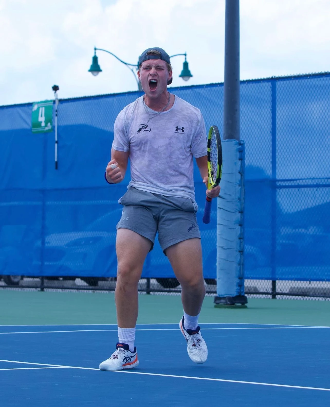 ESCA Alumni Andreas Scott player wearing gray outfit and cap celebrates with clenched fist and open mouth on a blue court.