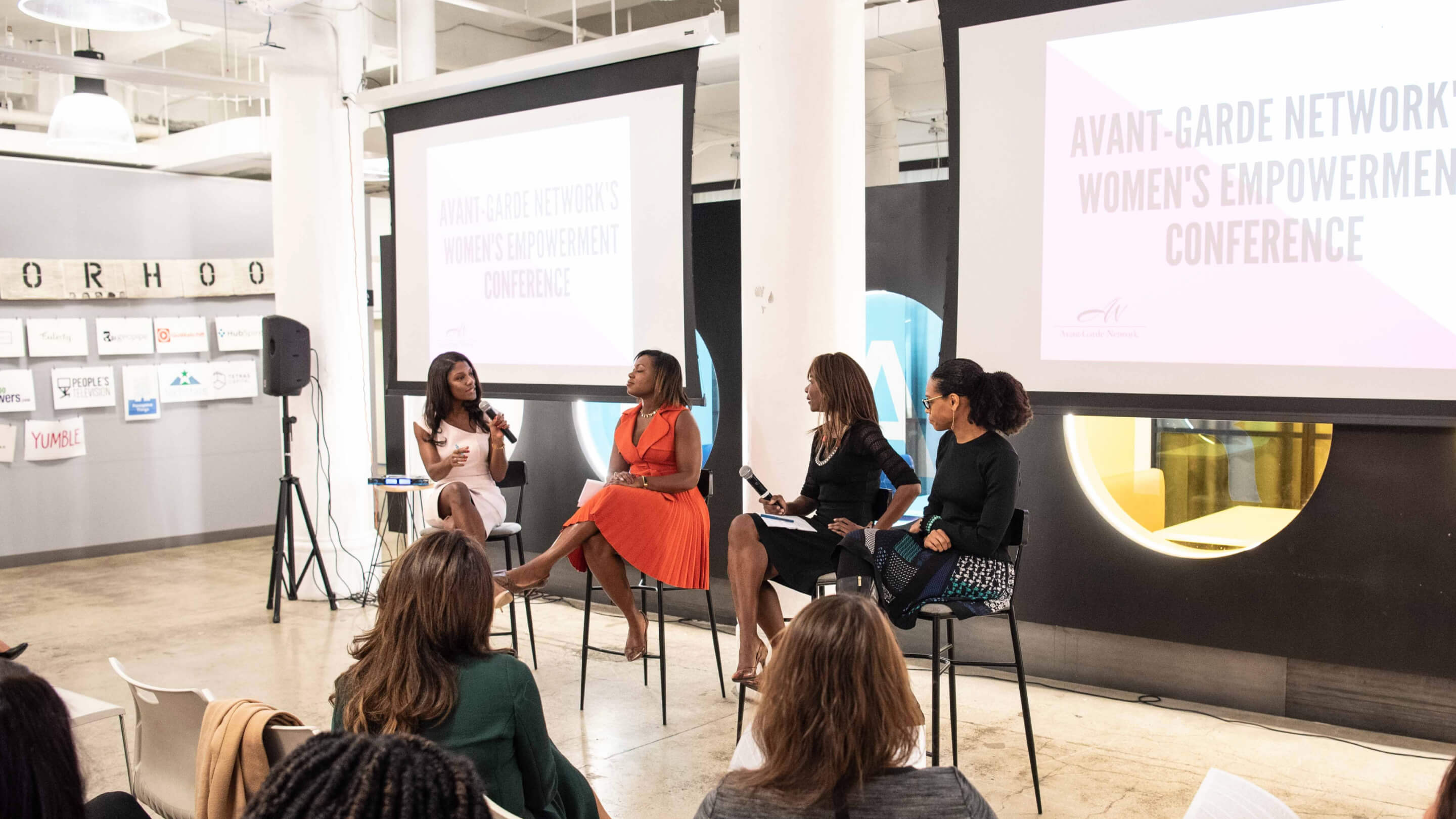 Four women on tall stools in a panel discussion at a women’s empowerment conference.