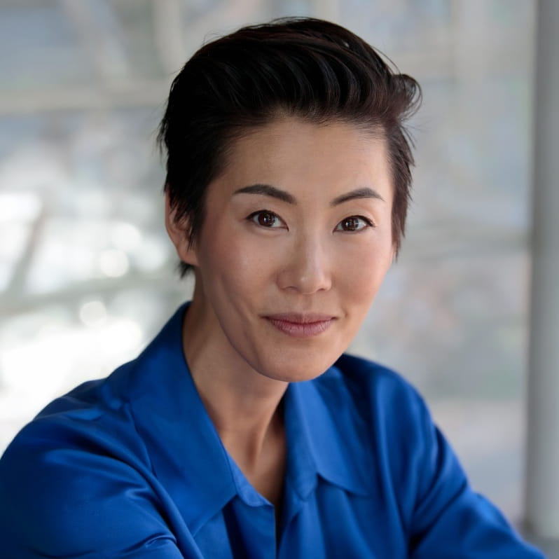 Smiling Asian woman with short dark hair wearing a blue shirt against a blurred background.