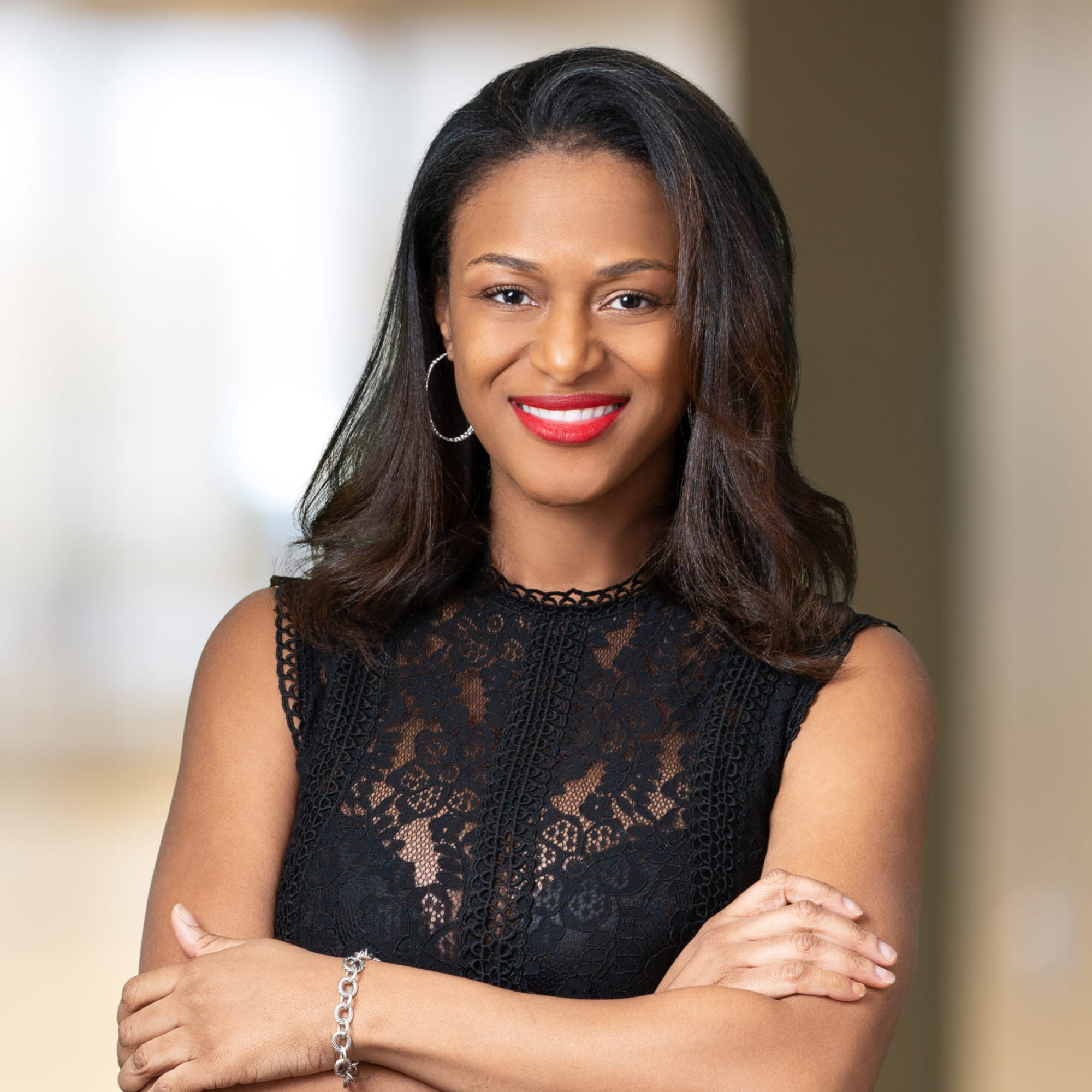 Smiling woman with shoulder-length hair wearing black lace top and red lipstick with arms crossed.