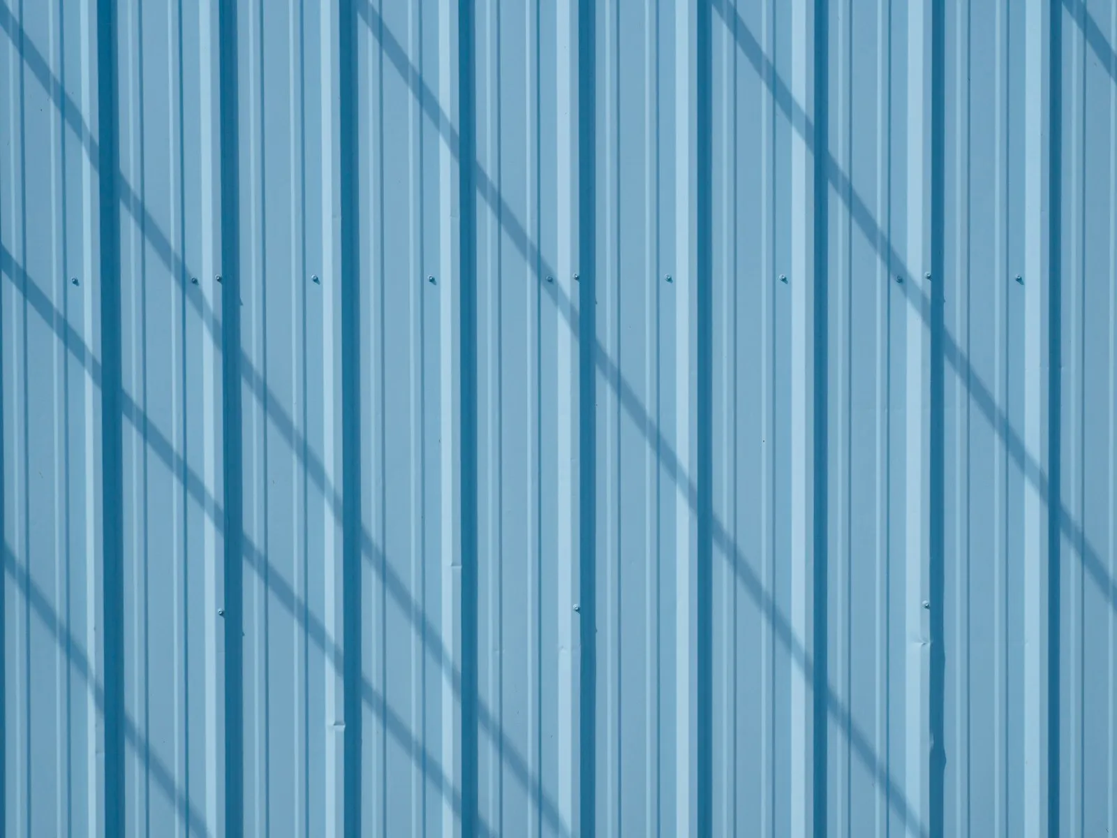 Des ombres traversent les nervures d’une façade métallique bleue.