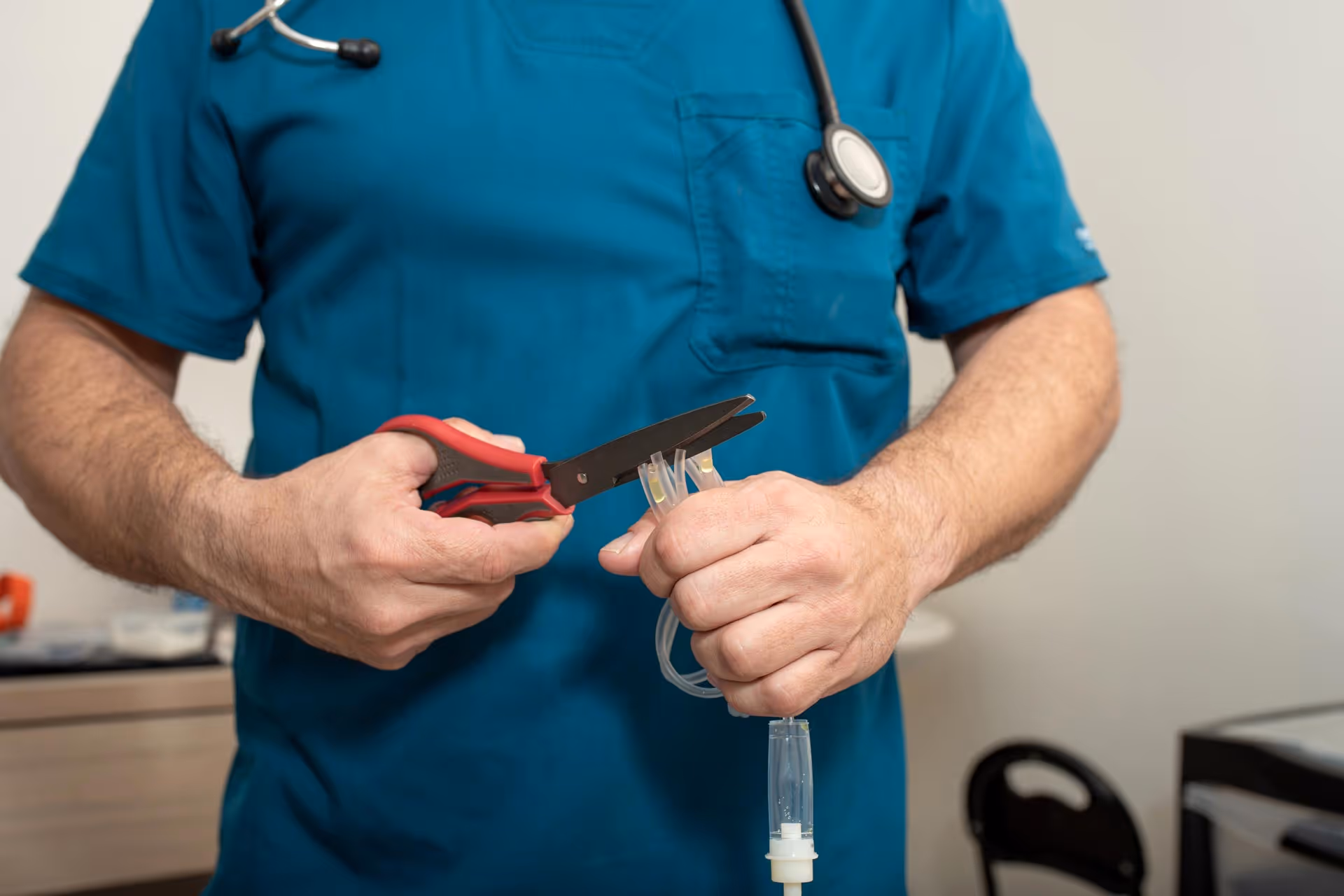 Healthcare professional in blue scrubs holding scissors and preparing medical tubing.