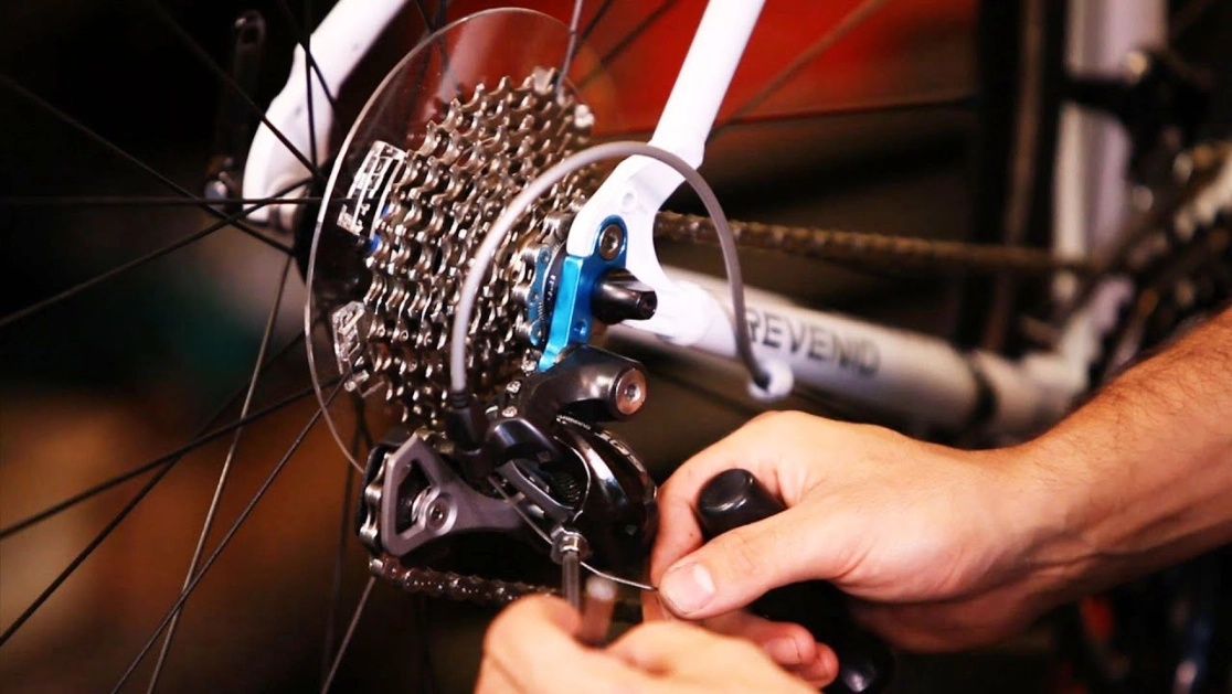 Person adjusting the rear derailleur gears on a white bicycle.