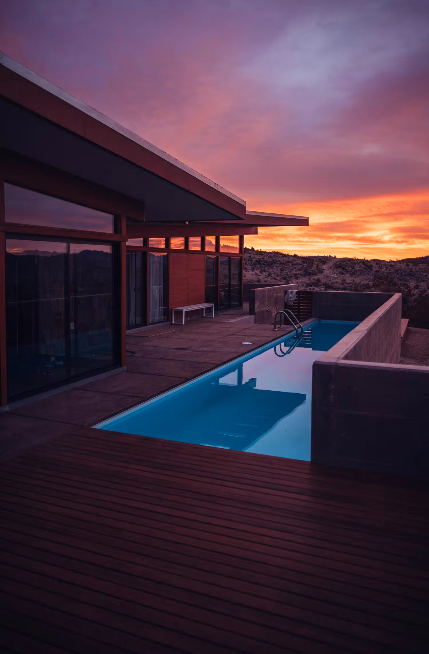 Casa moderna con una piscina alargada al aire libre durante un atardecer con cielo púrpura y naranja.